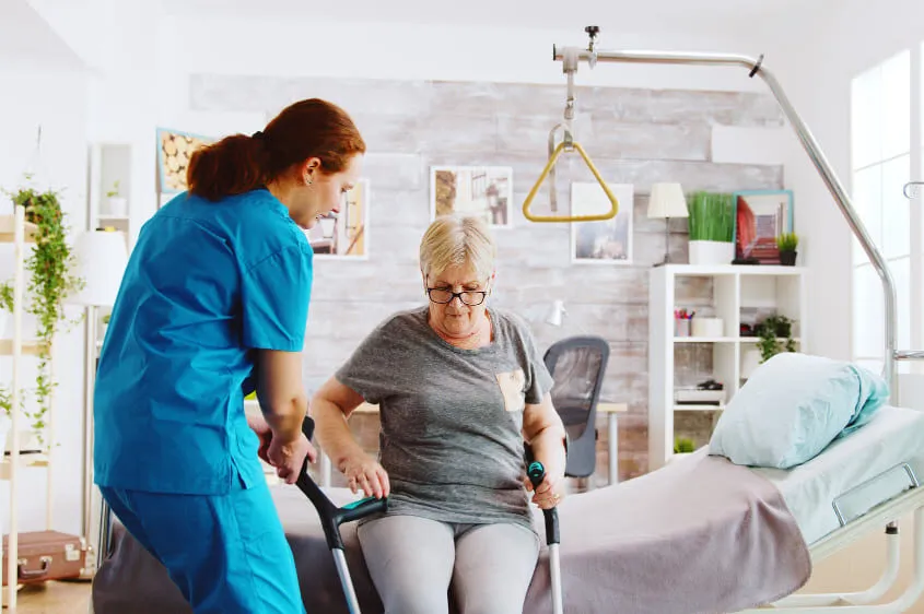 old-disabled-lady-walking-with-the-help-of-crutches-in-nursing-home-while-nurse-is-takinh-care-of-her (1)